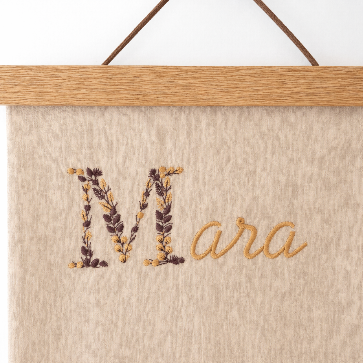 Prénom brodé sur une affiche de naissance en coton et suspendu par des baguettes en bois aimantées